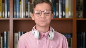 Footage portrait shot of the cute schoolboy standing near the bookshelf in the library. 4k video