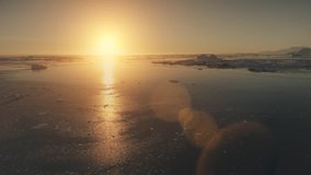 Antarctica sunset. Epic aerial view drone flight. Fast time lapse shot over the ocean water and glacier ice. Orange sun light given bright beams. 4k footage.