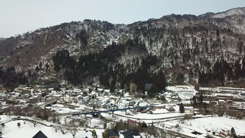 Aerial view of a train of JR Senzan Railway traveling across a bridge in Yamadera village in the valley and Risshaku-ji Buddhist Temple on mountainside in the snowy winter season in Yamagata, Japan