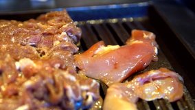 This close up video shows beef and chicken meats being placed and cooked on a sizzling grill.