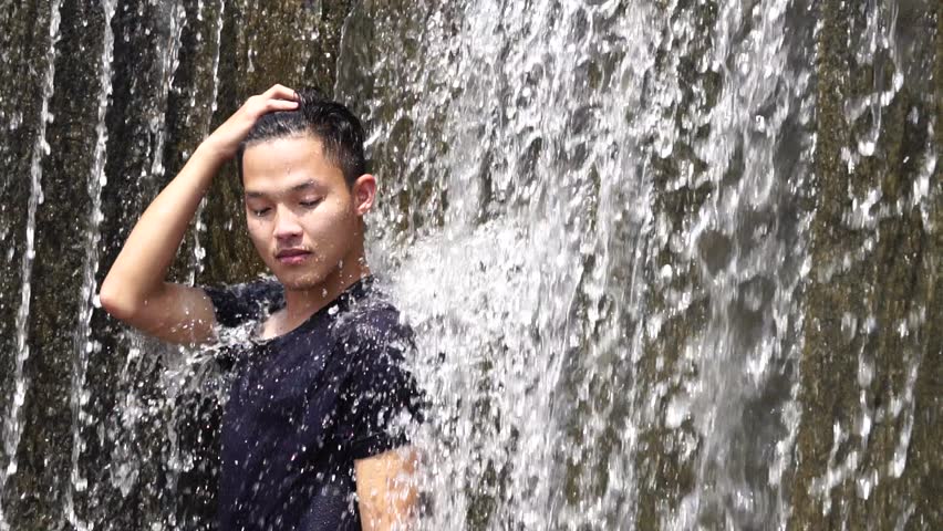 Asian smart Young man sitting relax post at waterfall Curtain splash in swimming pool with smiling on summer day. Relaxing for life natural therapy and refreshing Travel of Thailand