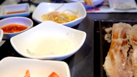 This close up panning video shows assorted side dishes and sizzling meat at korean bbq restaurant.