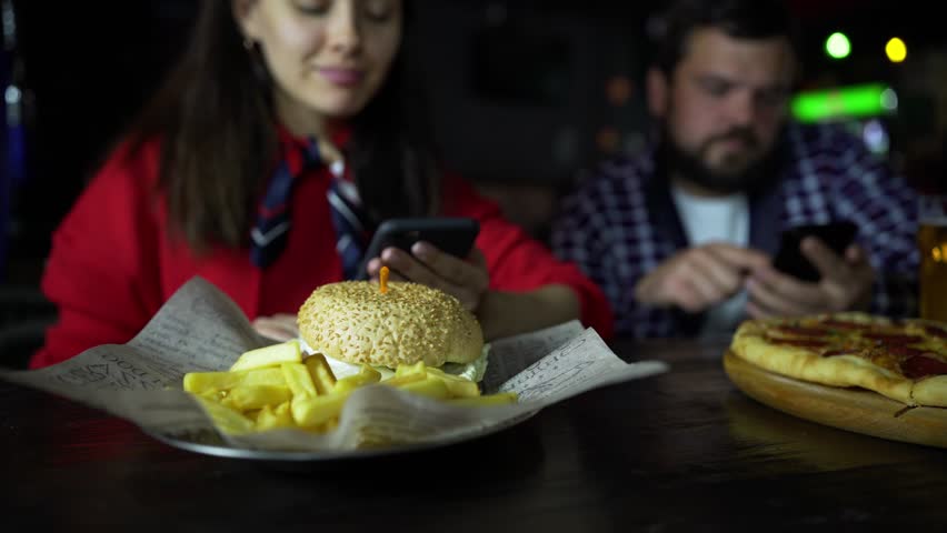 A girl in the company of a man taking pictures on your smartphone your Burger at the bar.
