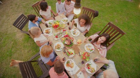 Big Family Garden Party Celebration, Gathered Together at the Table Relatives and Friends, Young and Elderly are Eating, Drinking, Passing Dishes, Joking and Having Fun. Top Down Camera Shot.