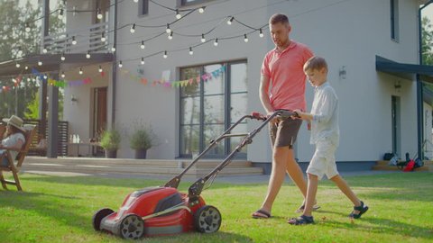 Good Father Teaches Son How to Use Walk Behind Lawn Mower, They Push it Together, Cutting Grass. Family Spending Time Together on a Sunny Day.