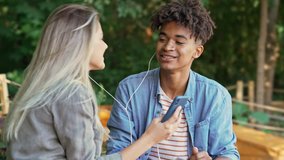 Pleased young multiethnic couple listening music by smartphone and singing while spending time together at the park
