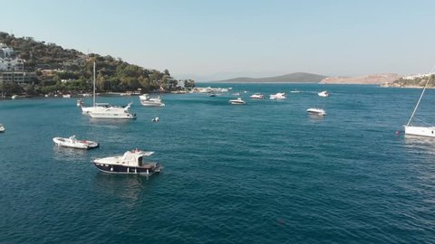 Sunny afternoon in small Aegean bay with anchored boats and luxury hotel in the background (4K aerial) 2