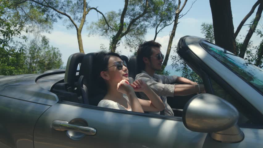young asian couple having fun driving and riding in convertible sport car on seaside road? Royalty-Free Stock Footage #1018063297