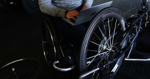 Disabled man using laptop while repairing wheelchair at workshop 4k