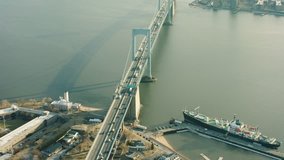 Aerial pan of Throgs Neck Bridge to vehicles driving along the bridge in New York City. Warm sunny lighting. Wide to medium shot. 4k shot with a RED camera.