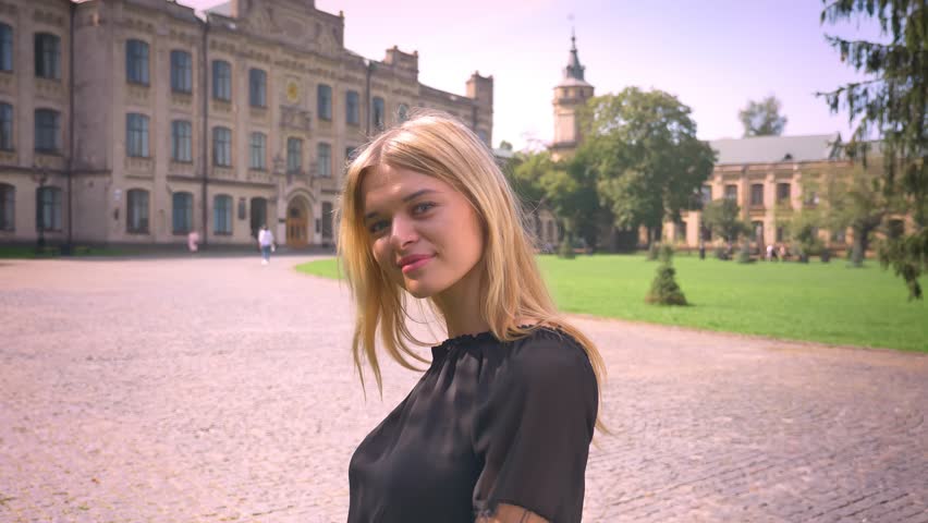 Awesome caucasian blonde girl in motion on city background and demonstrating like gesture with cute smile outdoor
