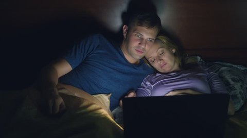 Couple, man and woman, watching a movie on a laptop on a bed in the bedroom before bed. watching a boring movie, falling asleep while watching a movie