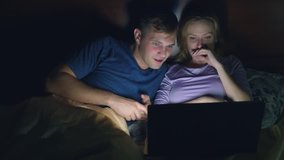 Couple, man and woman, watching a movie on a laptop on a bed in the bedroom before bed. watching an exciting movie, the audience is watching with interest, experiencing various emotions.