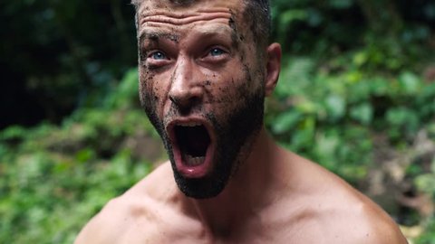 Close-up of a young handsome screaming man with dirty face in a wild forest 4K