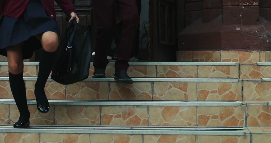 Close up of the feet of schoolboys and schoolgirls in the school uniforms running down the school stairs after classes. Outdoors.