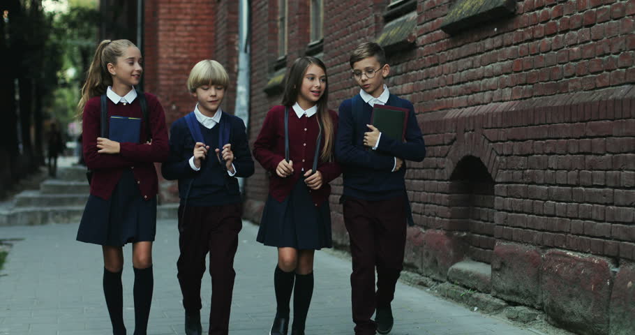 Group of schoolchildren in the uniforms going to the school in the morning and walking the street while chatting.