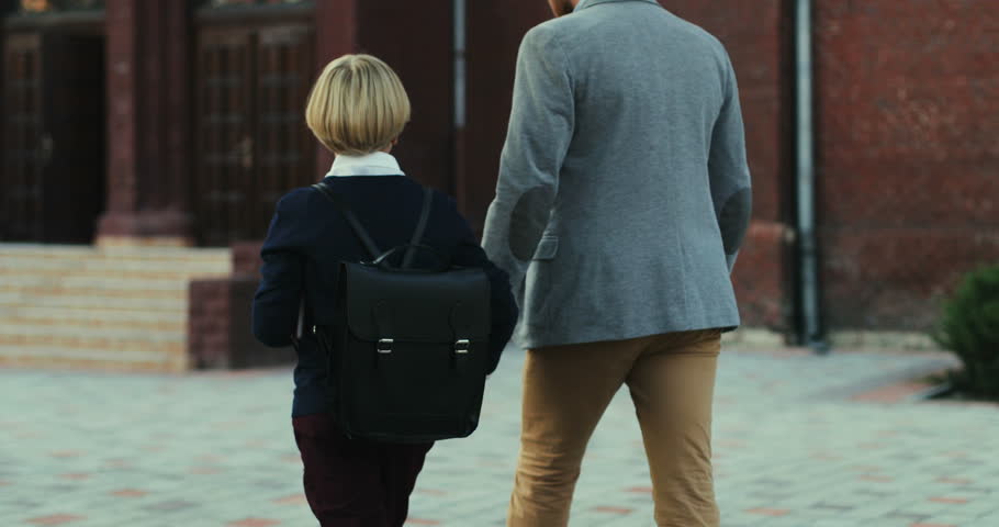 Back view on the caucasian father walking with his son when bringing him to school in the morning. Rear.