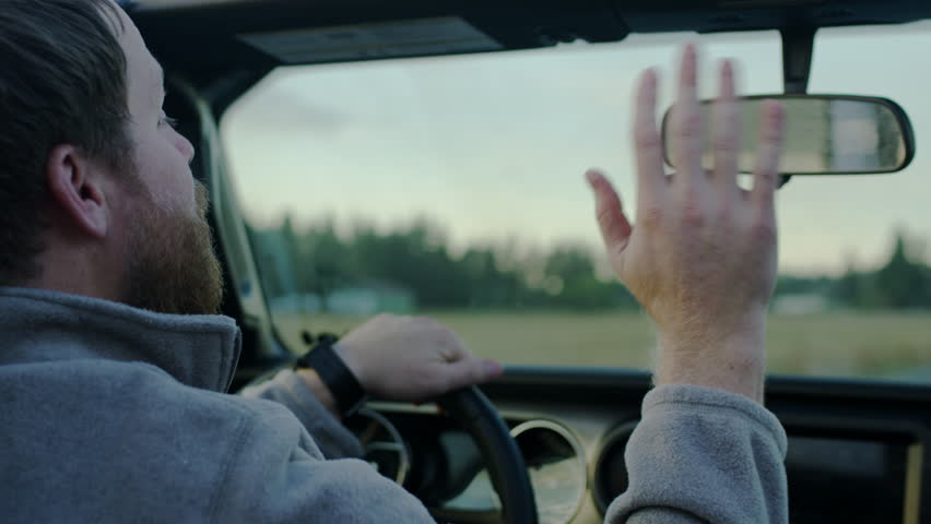 Closeup Of Dad Driving, He Adjusts His Rear View Mirror And Waves To Child In Back Seat, Slow Motion