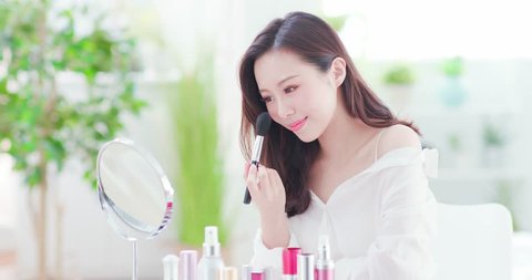 Smile woman with makeup brushes near face and look mirror at home
