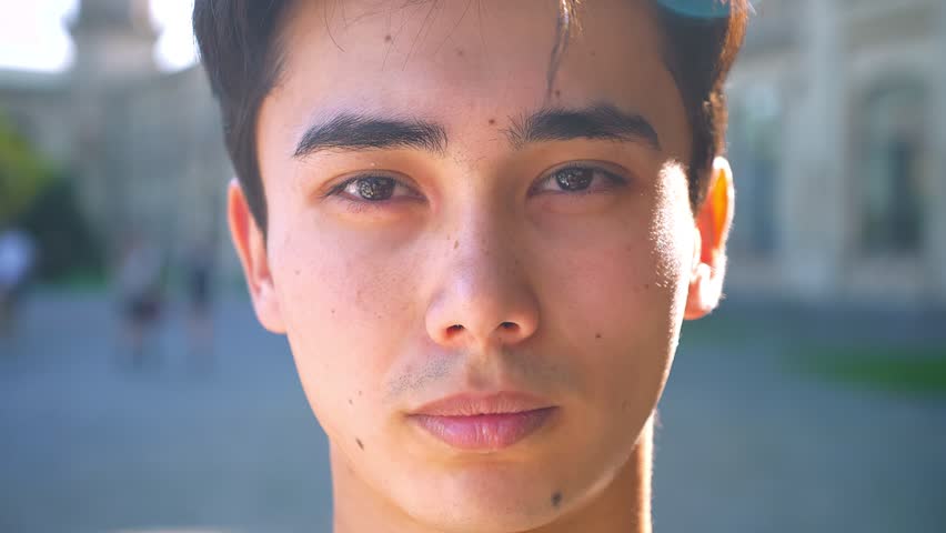 Close-up portrait of asian male looking at camera straight, serious concentrated mood in shadow, summer outdoor | Shutterstock HD Video #1018093183