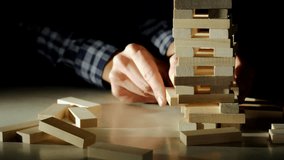 Business risks in the business. Jenga falls on the table, the tower falls. Slow motion video. Male hand pulls out a wooden brick and construction collapses