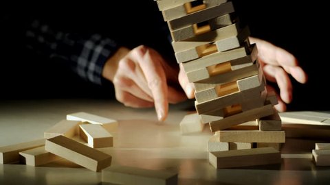Business risks in the business. Jenga falls on the table, the tower falls. Slow motion video. Male hand pulls out a wooden brick and construction collapses