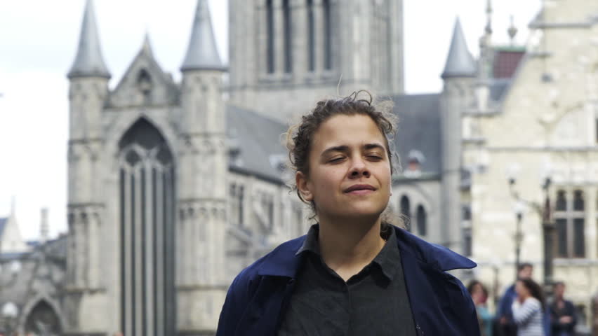 Woman walking on St. Michael Bridge in Ghent. Portrait of young girl enjoing view of ancient town,unrecognizable people moving at blurred background