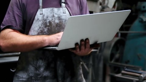 Front view Close up of smiling Caucasian blacksmith using laptop in workshop 