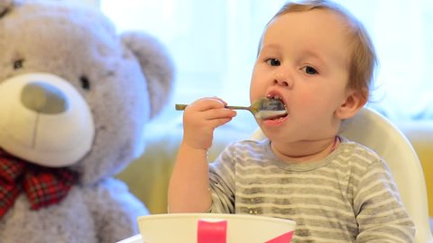 Young baby learning to eat with spoon. Infant baby eating. 
