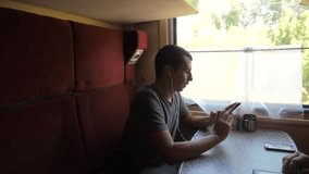 silhouette of man on a train railway car listening to music on headphones writing a message in a lifestyle messenger social media smartphone. slow motion video travel by train . man with smartphones