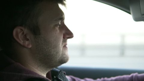 A man driving a car. His eyes are closing. He looks very tired from a long road