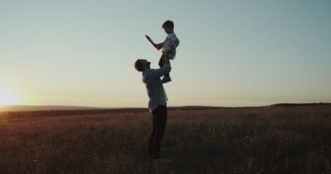 Awesome moments between dad and son , playing together and spending a good time together at sunset in the middle of field.