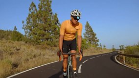 Tracking video shot of a male cyclist climbing up a mountain road. Man doing cycling training on a hilly highway road on a sunny day.