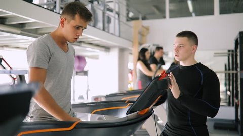 Young fitness instructor coaching beginner man while he running on treadmill