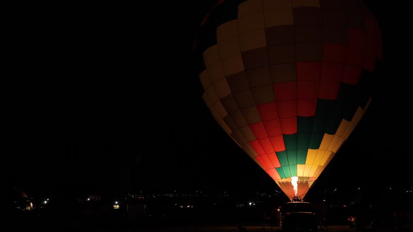 A hot air balloon fires up on a field at night for a balloon glow at a festival