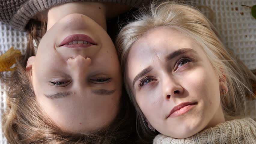 Closeup faces portrait of two young female girlfriends lying on rug smiling and talking