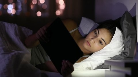 Serious teen browsing and watching media in a tablet lying on a bed at home