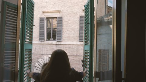 Female opens shutters of old window looking to the street of old Italian town