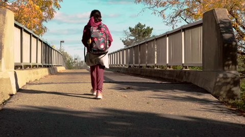 Student with backpack crossing bridge. Female student on her way home from school crossing overpass on a sunny autumn afternoon. Suited for use as green screen background plate.