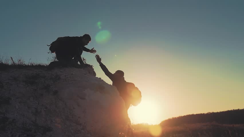 Silhouette of helping hand between two climber. two hikers on top of the mountain, a man helps a man to climb a sheer stone. couple hiking help each other silhouette in mountains with sunlight. Royalty-Free Stock Footage #1018162975