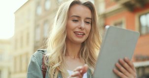 Close up of the blonde attractive young woman walking the city street and having a videochat on the tablet device.