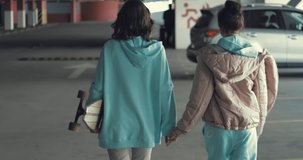Two happy teen girls reunited in car parking hugging and walking home hand in hand. Urban city lifestyle. 4K video shooting by handheld gimbal