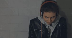 Urban girl using mobile phone. Young caucasian woman sitting on skateboard listening to music on smartphone late at night in dark underground tunnel. 4K video shooting by handheld gimbal