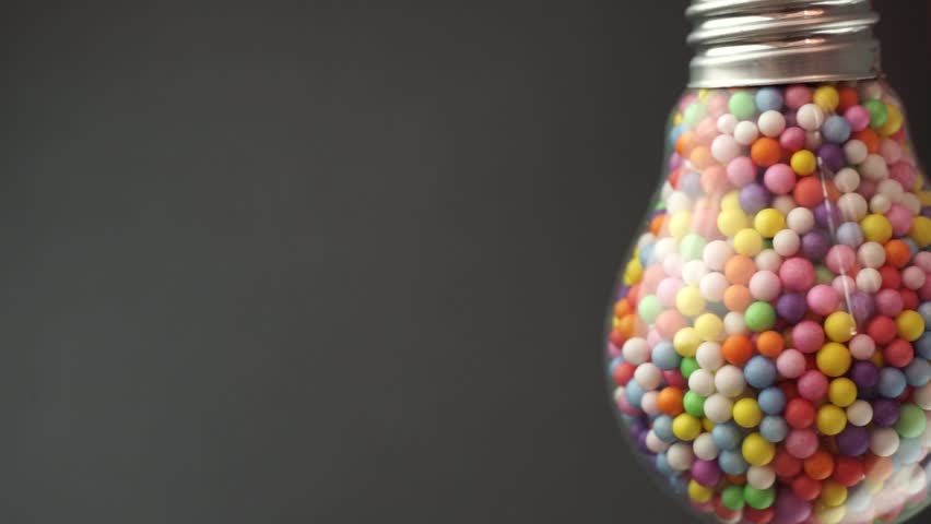 Lightbulb filled with colored ball dark background, macro view. Best idea concept.