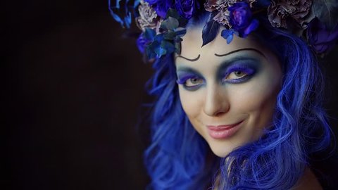 Halloween face art. Portrait of a beautiful woman looking at the camera and smiling, makeup the bride's corpse. Blue accents on hair and eyes, black background