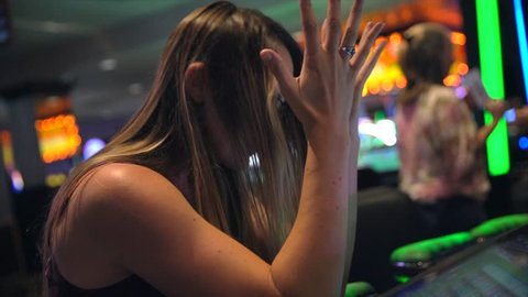 This video shows a young caucasian woman disappointed as she loses money on slot machines while gambling at a casino.
