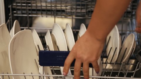 Female hands putting big and small white plates in the dishwasher. Woman closes dishwasher after loading.