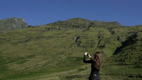 Girl taking pictures and panoramic video of green mountains in French Pyrenees on a smartphone. High hills and blue sky.