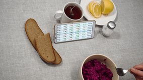 Businesswoman having lunch. On the table is a salad, bread, lemon and tea. She watches online currency quotes on the smartphone screen. Focus on smartphone screen. - Powered by Shutterstock - Get 15% off with code: PIKWIZARD15