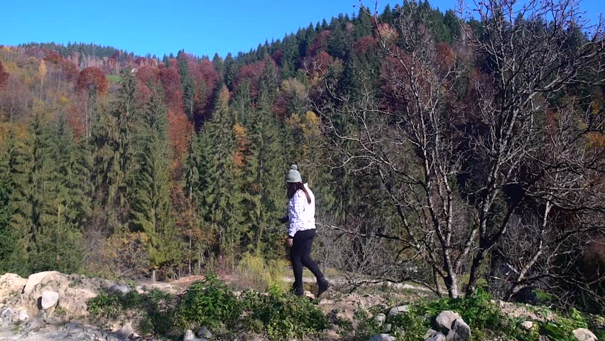 a beautiful girl in a white jacket and hats walking along the background of the autumn mountains